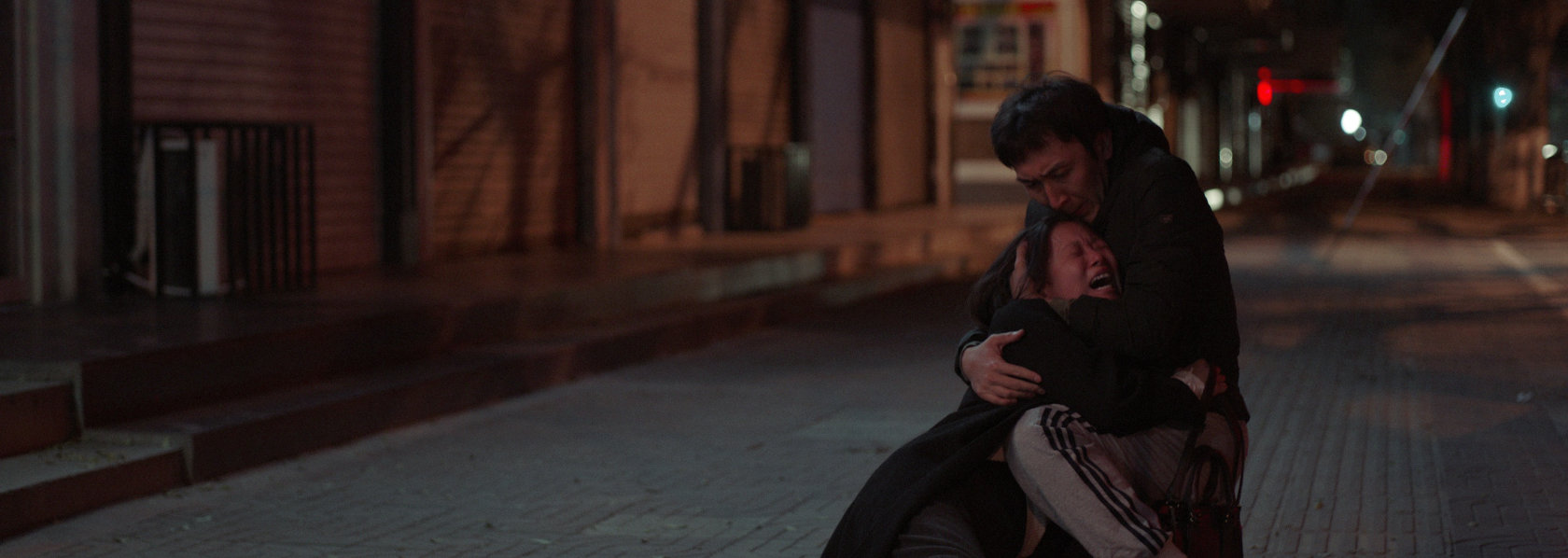 A man kneeling on the floor hugging a wailing woman in the street - Lost Lotus - THIS Buddhist Film Festival