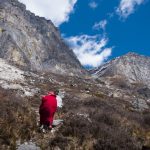 Backview of person in red robes and hat walking up a mountain - Wandering But Not Lost - THIS Buddhist Film Festival