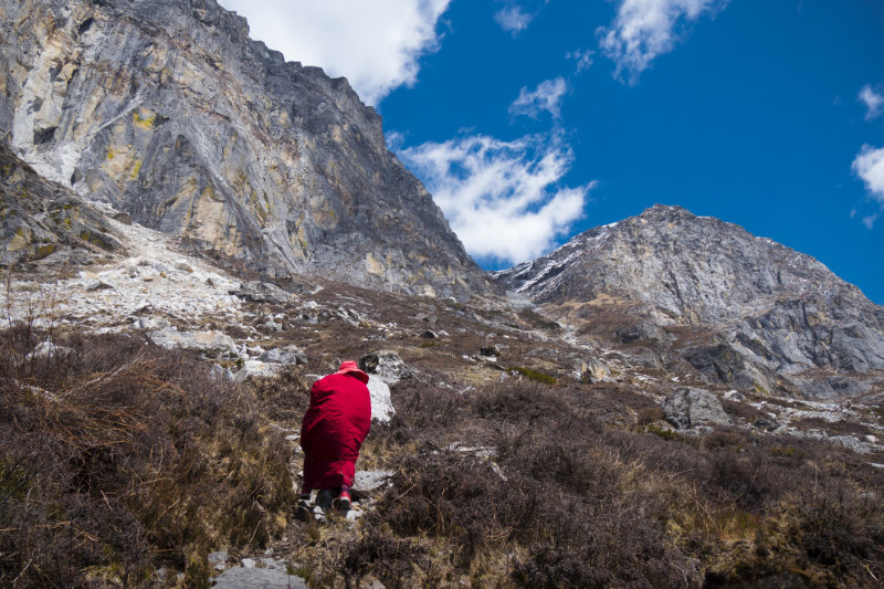 Backview of person in red robes and hat walking up a mountain - Wandering But Not Lost - THIS Buddhist Film Festival