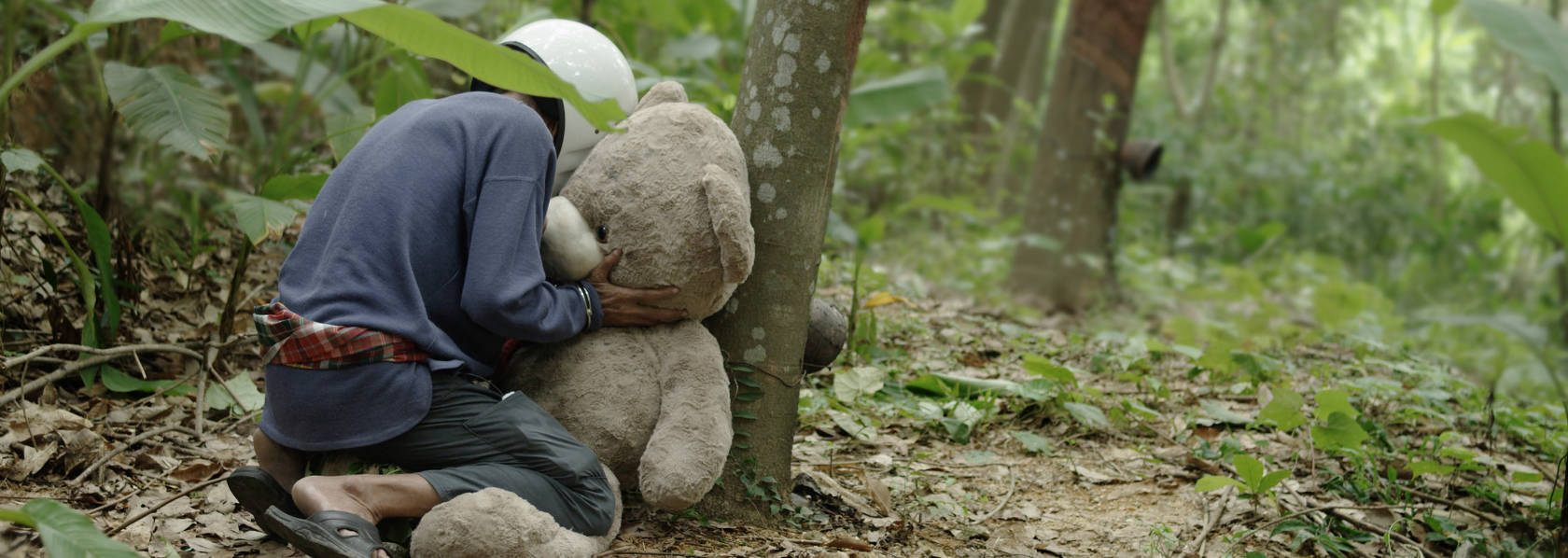 VANISHING POINT - Backview of man with helmet hugging a teddy bear in the forest - THIS Buddhist Film Festival